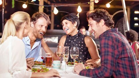 Vier Personen sitzen lachend beim Abendessen am Tisch 