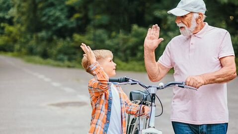 Opa und Enkel stehen um ein Fahrrad und klatschen sich ab