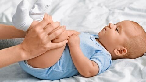 Zwei Hände greifen einem auf dem Rücken liegenden Baby an die Beine
