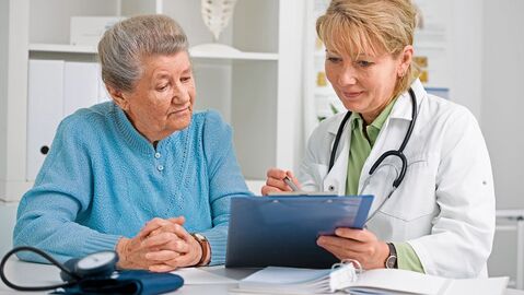 Ärztin zeigt einer älteren Dame etwas auf einem Klemmbrett