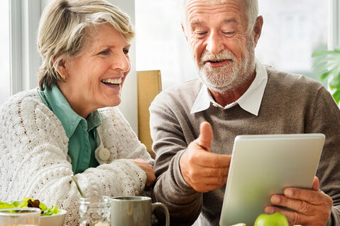 Lachender Mann zeigt begeisterter Frau etwas auf einem Tablet