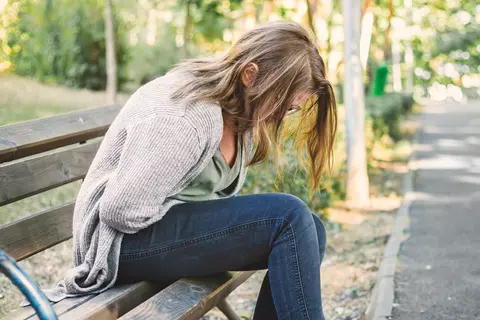 Frau sitzt mit Bauchkrämpfen auf einer Bank im Park
