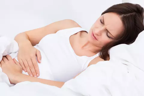 Frau mit Bauchschmerzen liegt im Bett und hält sich den Unterbauch.