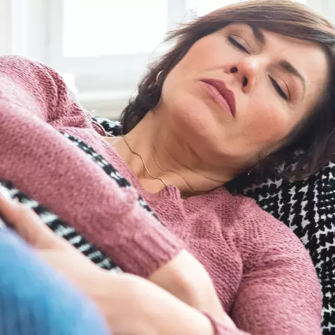 Eine Frau mit Bauchschmerzen auf dem Sofa 