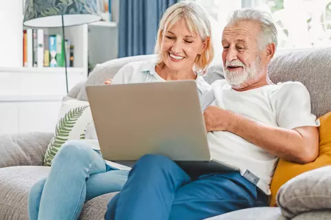 Mann und Frau sitzen lachend auf einem Sofa und schauen sich auf dem Laptop den Ratgeber bei Darmbeschwerden an