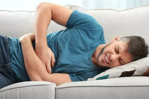 Mann mit Bauchschmerzen liegt auf dem Sofa und hält sich den Bauch