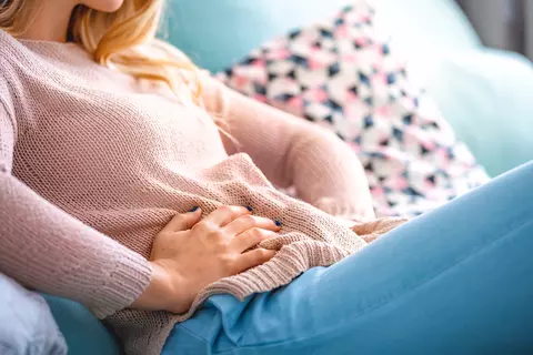Frau mit Blähungen sitzt auf dem Sofa und hält sich den Bauch