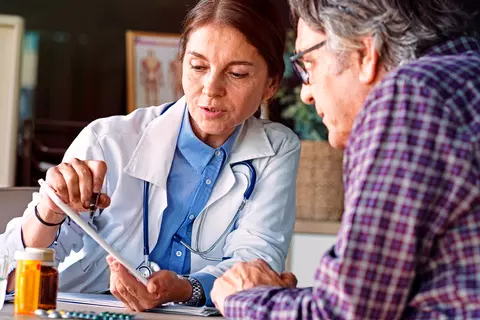 Ärztin zeigt ihrem Patienten etwas auf einem Tablet und geht mir ihm die Symptome eines Reizmagen durch