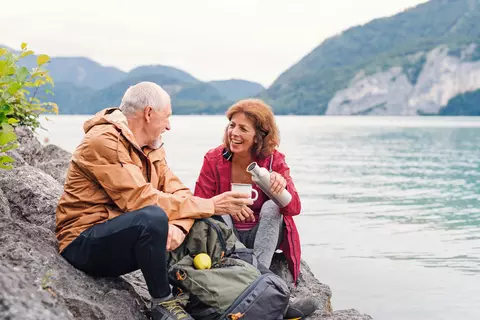 Frau und Mann sitzen am See und machen eine Trinkpause bei einer Wanderung