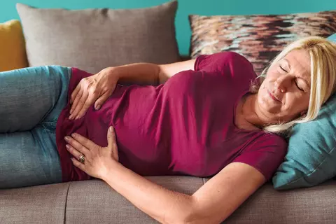 Frau liegt mit geschlossenen Augen auf der Couch und hält sich am Bauch