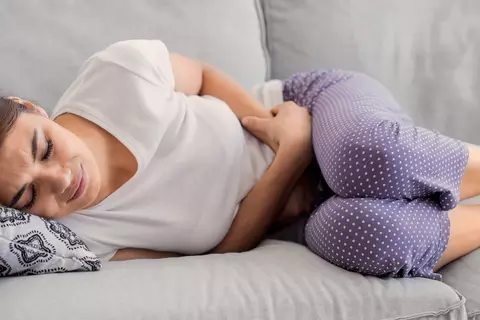 Frau liegt auf der Couch und krümmt sich vor Bauchschmerzen