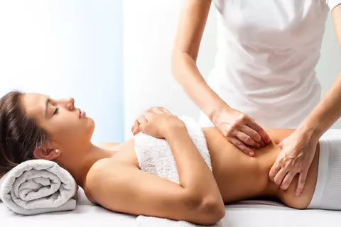 Frau auf einer Liege bekommt eine Bauchmassage