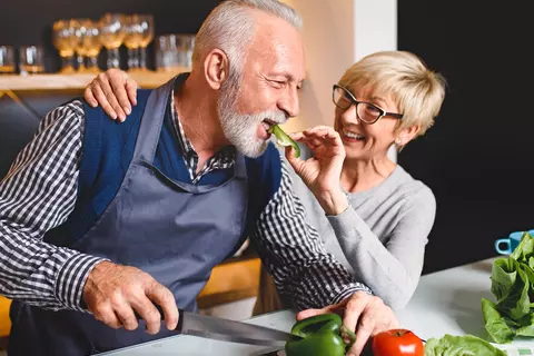 Frau gibt ihrem Mann etwas von der Paprika während des Kochens