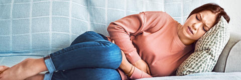 Frau liegt auf der Couch und umklammert ihren schmerzenden Bauch aufgrund eines Reizmagen
