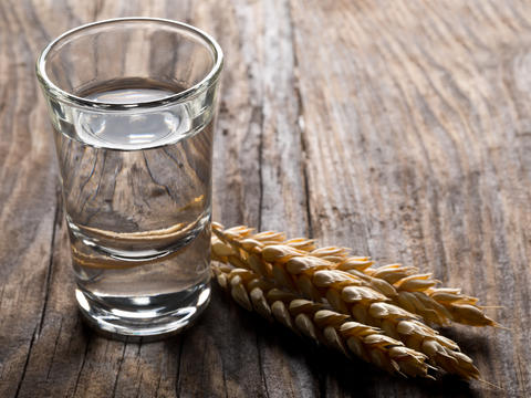 Gefülltes Schnapsglas mit einer Kornähre auf iener hölzernen Tischplatte