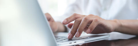 Die Hände einer Frau, die auf der Tastatur eines Laptops tippt